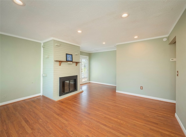 unfurnished living room with hardwood / wood-style floors, ornamental molding, a textured ceiling, and a brick fireplace