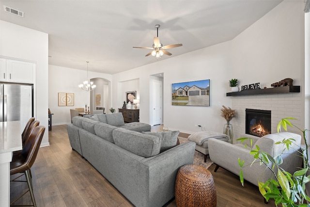 living room with dark hardwood / wood-style flooring, ceiling fan with notable chandelier, and a fireplace