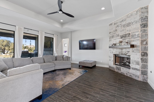 living room featuring a raised ceiling, ceiling fan, a fireplace, and dark hardwood / wood-style floors