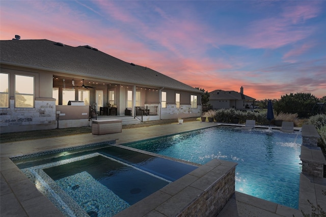 pool at dusk with a patio area, ceiling fan, pool water feature, area for grilling, and an in ground hot tub