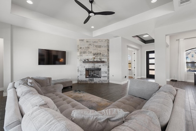 living room with dark hardwood / wood-style flooring, a raised ceiling, ceiling fan, and a stone fireplace