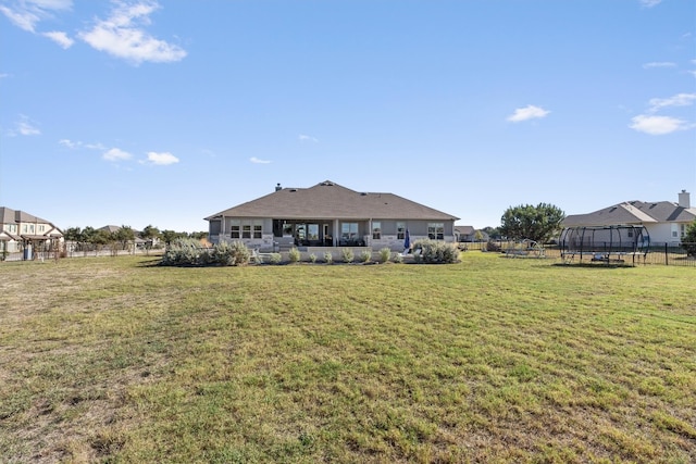 rear view of house with a lawn and a trampoline