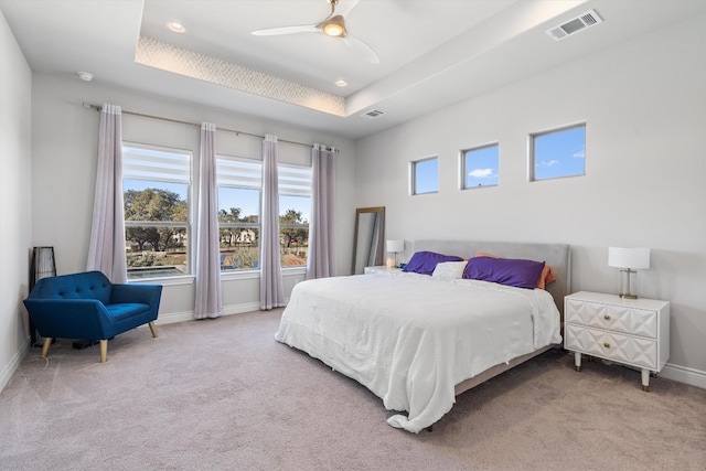 carpeted bedroom with a raised ceiling and ceiling fan