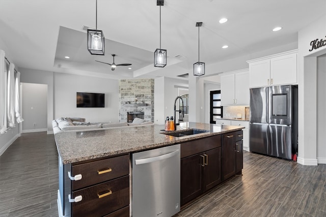 kitchen with dark wood-type flooring, a stone fireplace, sink, ceiling fan, and appliances with stainless steel finishes