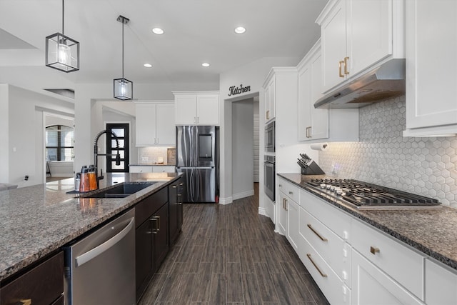 kitchen with appliances with stainless steel finishes, sink, dark stone countertops, white cabinetry, and hanging light fixtures