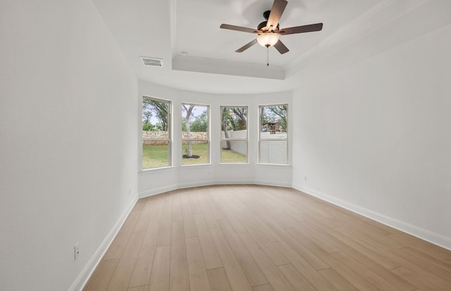spare room featuring a ceiling fan, visible vents, a raised ceiling, baseboards, and light wood finished floors