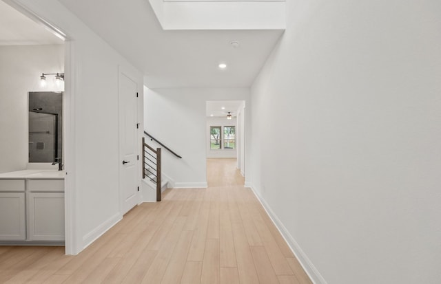 hall with light wood-style floors, a skylight, recessed lighting, and stairs