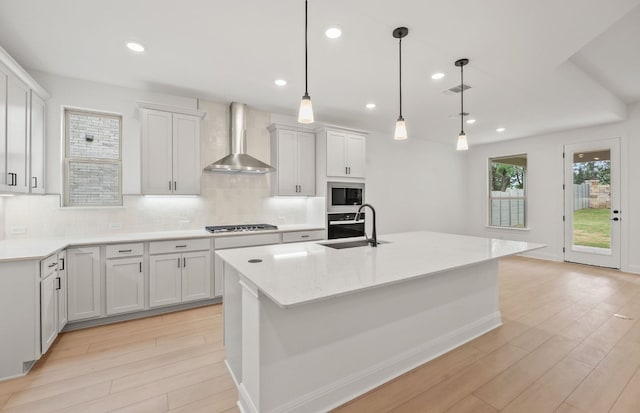 kitchen with a sink, light wood-style floors, stainless steel gas cooktop, wall chimney exhaust hood, and backsplash