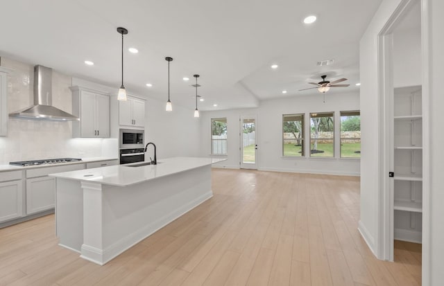 kitchen with wall chimney range hood, a sink, built in microwave, backsplash, and visible vents
