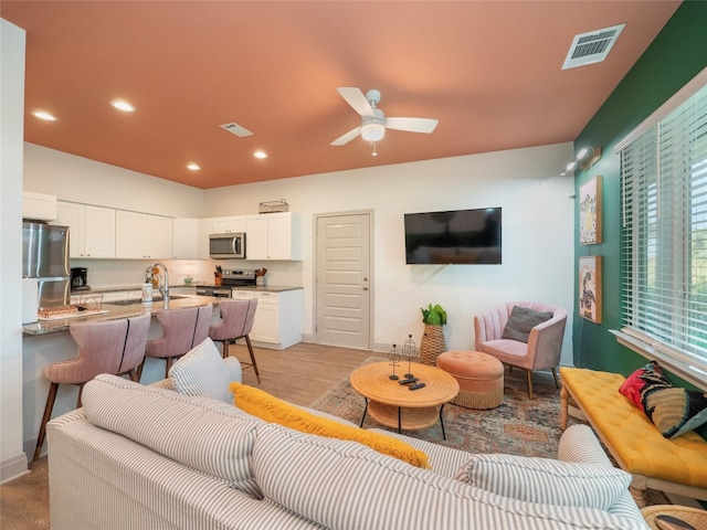 living room with ceiling fan, light wood-type flooring, and sink