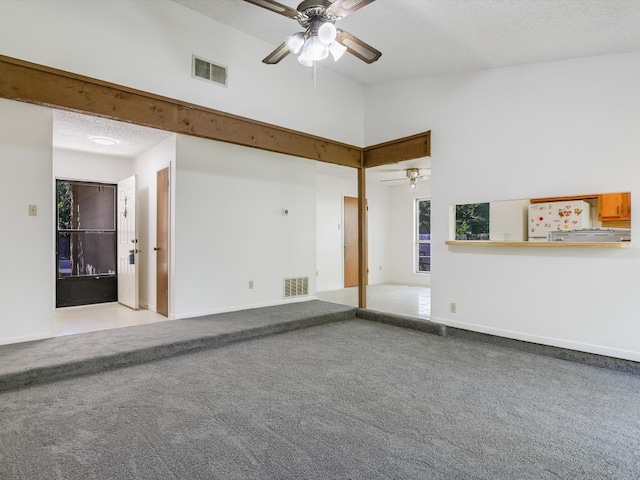 carpeted empty room featuring a towering ceiling, a textured ceiling, a wealth of natural light, and ceiling fan