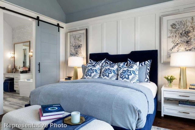 bedroom with a barn door, ensuite bath, dark wood-type flooring, and lofted ceiling