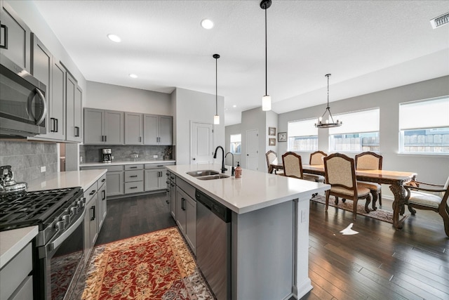 kitchen featuring appliances with stainless steel finishes, dark hardwood / wood-style flooring, sink, a center island with sink, and hanging light fixtures