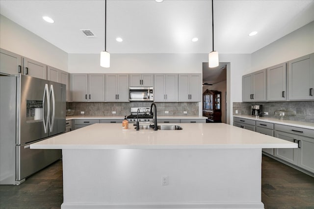 kitchen with a kitchen island with sink, dark wood-type flooring, sink, tasteful backsplash, and stainless steel appliances