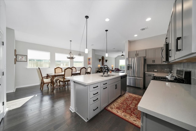 kitchen with sink, dark hardwood / wood-style floors, an island with sink, pendant lighting, and appliances with stainless steel finishes