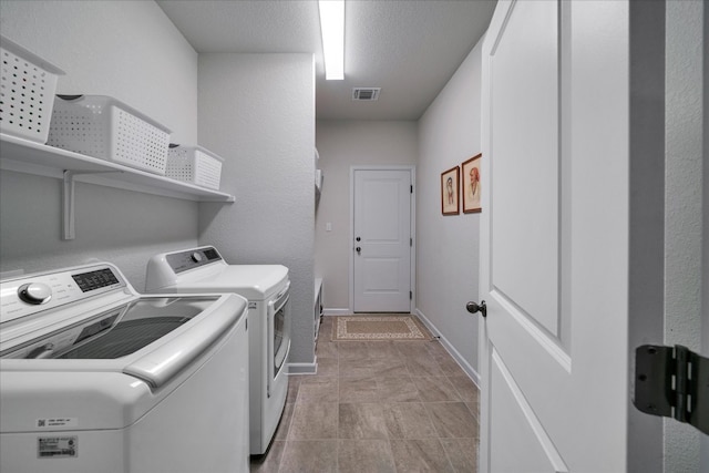 laundry area with a textured ceiling, washing machine and dryer, and light tile patterned floors