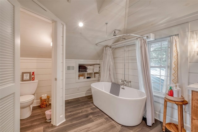 bathroom featuring lofted ceiling, a bathing tub, wooden walls, toilet, and wood-type flooring