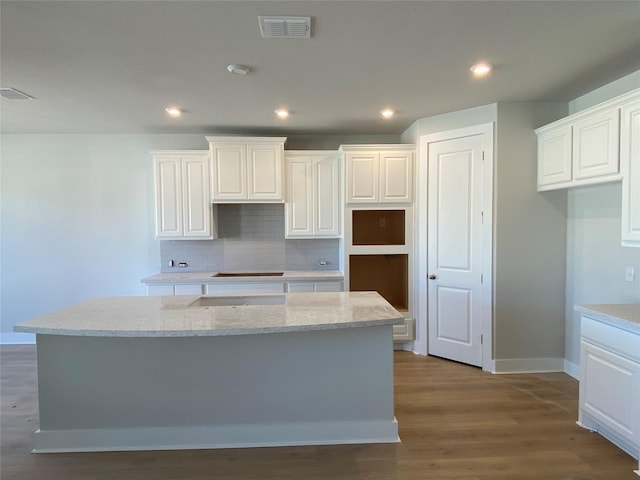 kitchen featuring white cabinetry, a center island, decorative backsplash, and light stone countertops