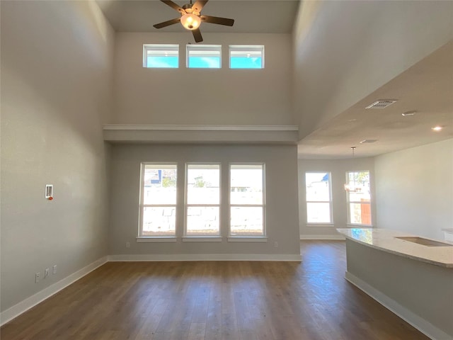 unfurnished living room with a high ceiling, dark hardwood / wood-style flooring, a wealth of natural light, and ceiling fan with notable chandelier