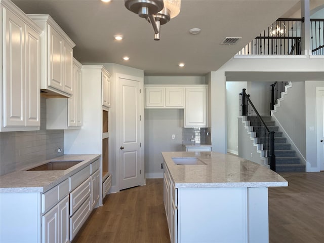 kitchen with white cabinets, light stone counters, tasteful backsplash, a kitchen island, and dark hardwood / wood-style flooring