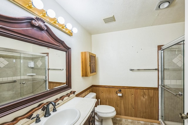 bathroom with vanity, toilet, a shower with door, and wood walls