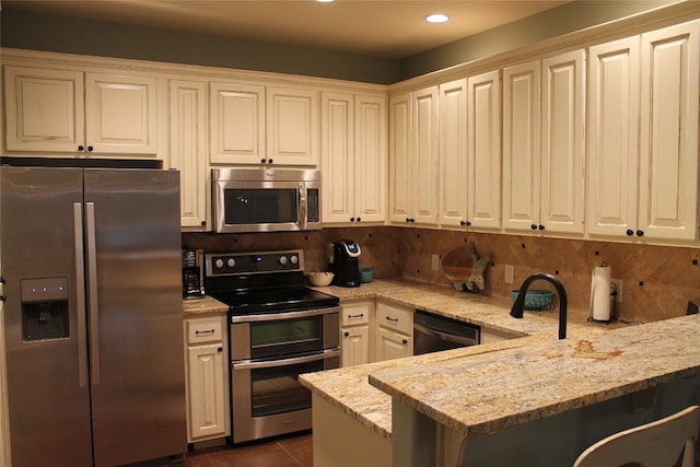 kitchen with backsplash, dark tile patterned floors, light stone counters, kitchen peninsula, and stainless steel appliances