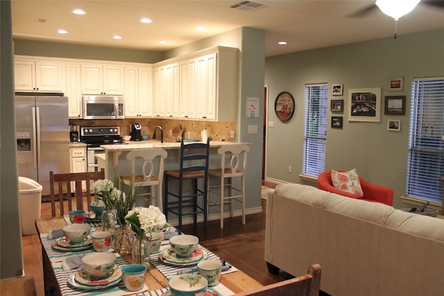 kitchen with a kitchen bar, appliances with stainless steel finishes, decorative backsplash, light stone countertops, and white cabinets