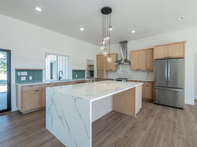 kitchen with wall chimney range hood, light wood-type flooring, decorative light fixtures, a kitchen island, and stainless steel appliances