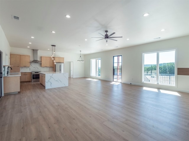 kitchen with stainless steel appliances, wall chimney range hood, light stone counters, decorative light fixtures, and light wood-type flooring