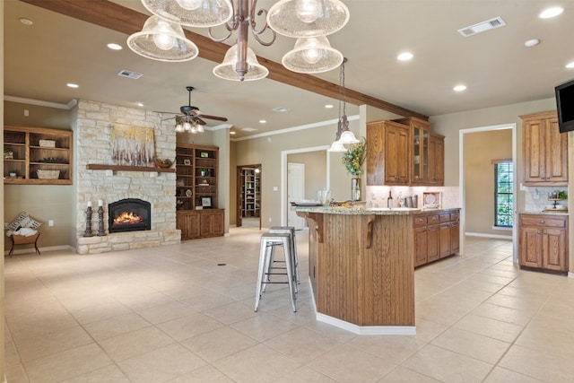 kitchen with ceiling fan, a fireplace, light stone counters, light tile patterned flooring, and a kitchen bar