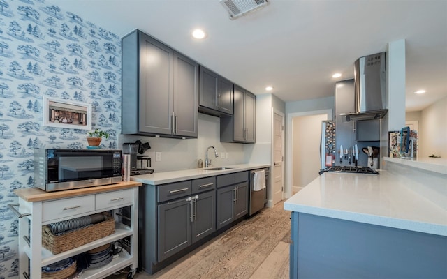 kitchen with gray cabinetry, wall chimney range hood, sink, light hardwood / wood-style floors, and stainless steel appliances