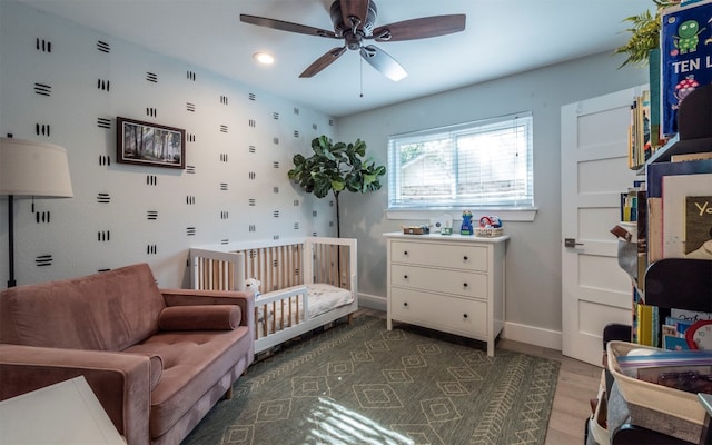 bedroom featuring ceiling fan, dark wood-type flooring, and a nursery area