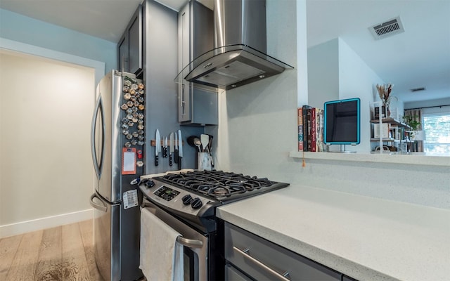 kitchen featuring gray cabinetry, light hardwood / wood-style floors, wall chimney range hood, and stainless steel appliances