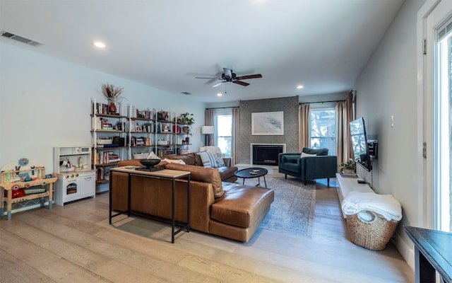 living room featuring ceiling fan, a large fireplace, and light hardwood / wood-style flooring