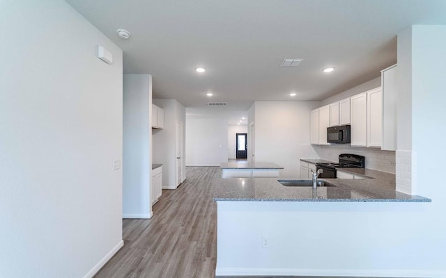 kitchen with kitchen peninsula, light stone counters, black appliances, white cabinets, and light hardwood / wood-style floors