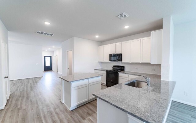 kitchen featuring kitchen peninsula, light stone countertops, sink, black appliances, and white cabinetry