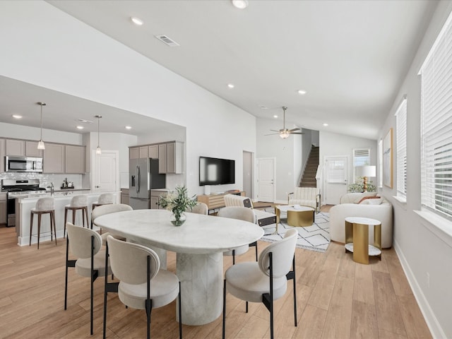 dining room with ceiling fan, light wood-type flooring, and high vaulted ceiling