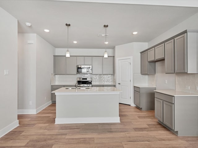 kitchen with gray cabinetry, an island with sink, light wood-type flooring, and appliances with stainless steel finishes