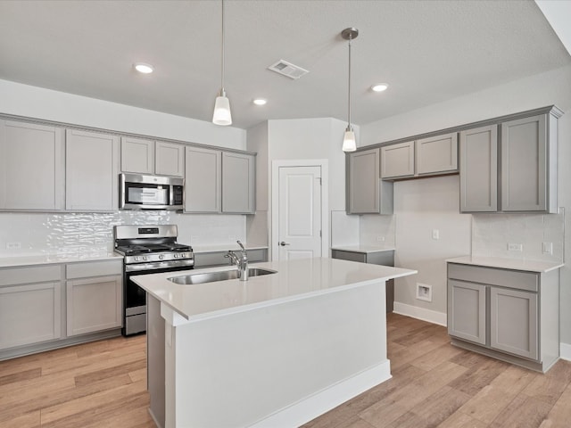 kitchen with light hardwood / wood-style floors, sink, stainless steel appliances, and a kitchen island with sink