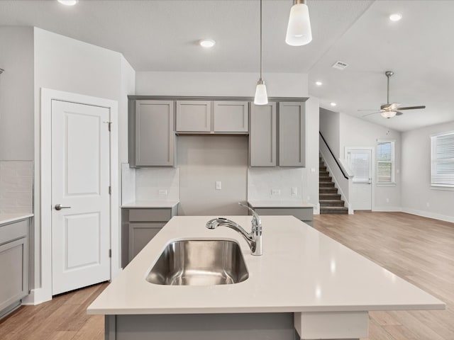 kitchen featuring light wood-type flooring, tasteful backsplash, sink, lofted ceiling, and an island with sink