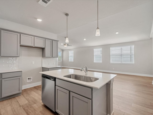 kitchen with gray cabinetry, sink, light hardwood / wood-style flooring, stainless steel dishwasher, and a center island with sink