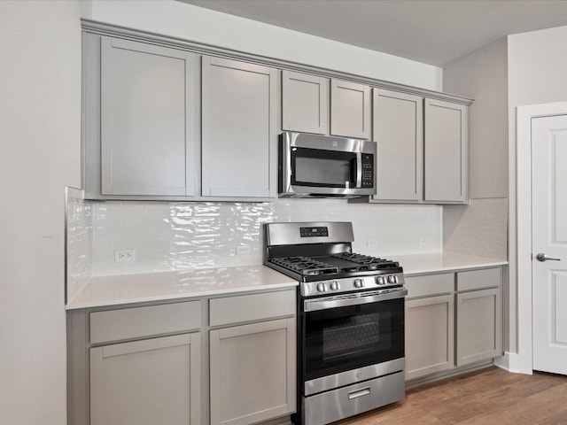 kitchen featuring backsplash, gray cabinetry, hardwood / wood-style floors, and stainless steel appliances