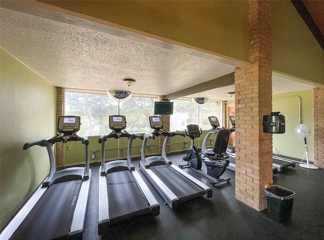 workout area with a textured ceiling, brick wall, and decorative columns