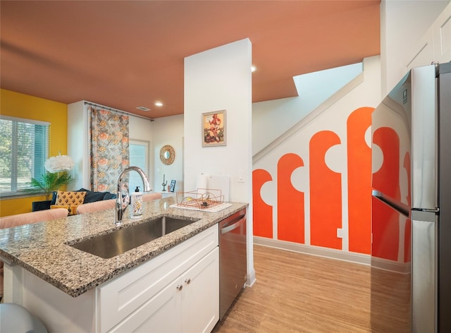 kitchen with appliances with stainless steel finishes, light stone counters, sink, white cabinets, and light hardwood / wood-style floors