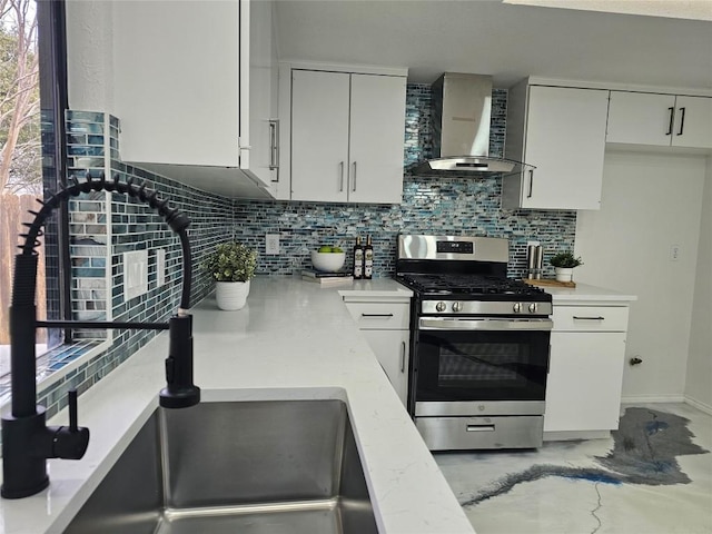 kitchen with concrete floors, white cabinets, wall chimney range hood, decorative backsplash, and stainless steel gas stove