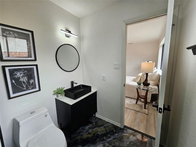 bathroom with a textured wall, toilet, connected bathroom, vanity, and baseboards