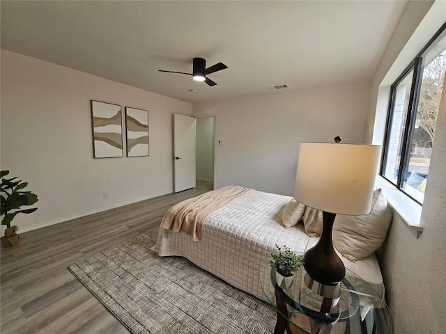 bedroom with ceiling fan, multiple windows, visible vents, and wood finished floors