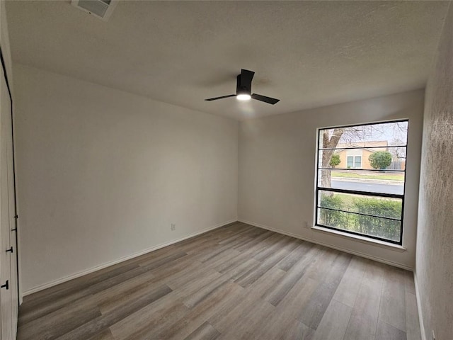 empty room with a ceiling fan, light wood-type flooring, visible vents, and baseboards