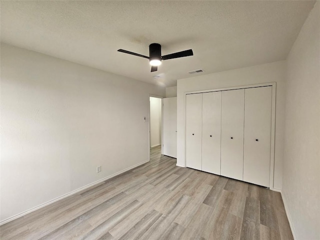 unfurnished bedroom featuring baseboards, visible vents, light wood-style flooring, a textured ceiling, and a closet