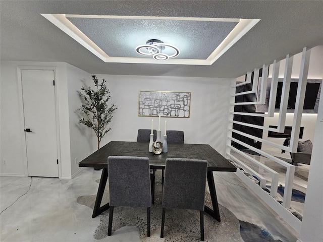 dining area with concrete flooring, a raised ceiling, and a textured ceiling